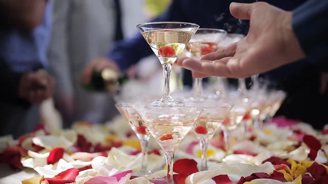 The guests' hands take glasses with bubbling wine at the party. Glasses are built in the pyramids. No recognizable persons