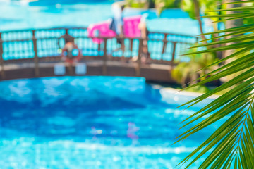 tropical summer background with palm tree, swimming pool and people walking on bridge