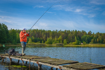 The young man catching fish on the lake from an aged pier.
