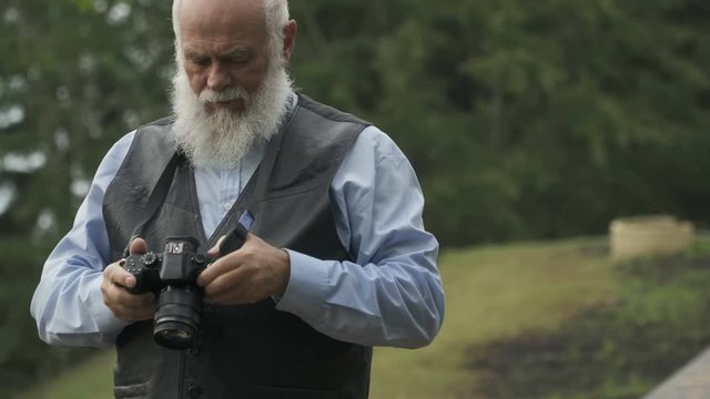 Gray-haired senior man photographs an autumn park