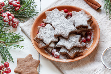 Traditional Christmas gingerbread cookies, stars in powdered sugar on the plate. Berries of red Rowan branch spruce.