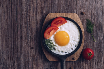 Fried eggs in a frying pan with fresh tomatoes on a wooden table, top view.
