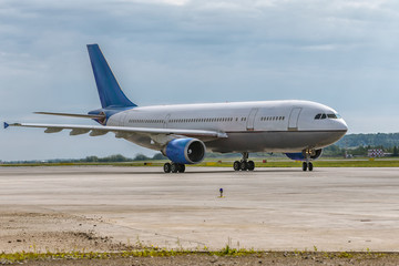 The airplane is moving on the runway against the background of the forest and blue cloud sky. Summer sunny weather