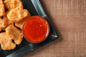 Plate with chicken nuggets and chili sauce on kitchen table