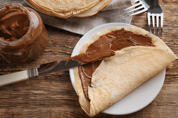 Delicious crepe with chocolate sauce on wooden table
