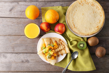 Delicious pancakes with fruits on wooden table