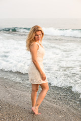 Fototapeta na wymiar Blonde woman in beige cocktail dress by the sea