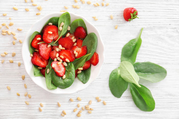 Plate of salad with spinach, strawberry and pine nuts on table