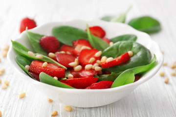Plate of salad with spinach, strawberry and pine nuts on table