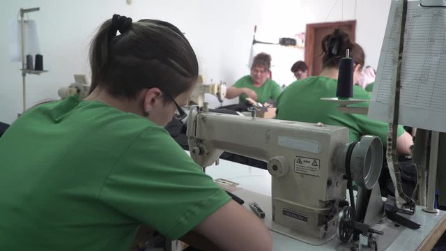 Caucasian girl sitting using sewing machine to stitching factory textile, close up, shallow depth of field, young female person tailoring, interior scene