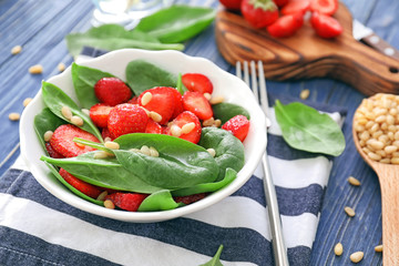 Plate of salad with spinach, strawberry and pine nuts on table