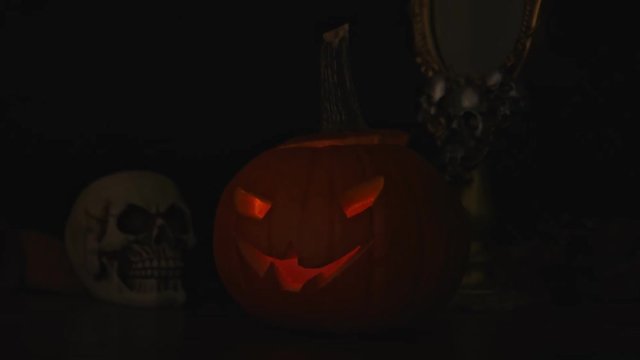 Carved Halloween pumpkin lights inside with flame and skuls around.