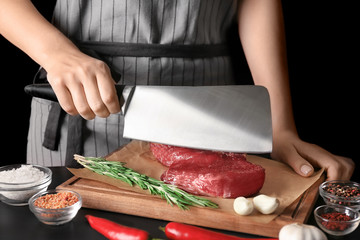 Woman cutting raw steak on kitchen table