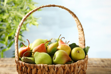 Wicker basket with ripe pears on table outdoors