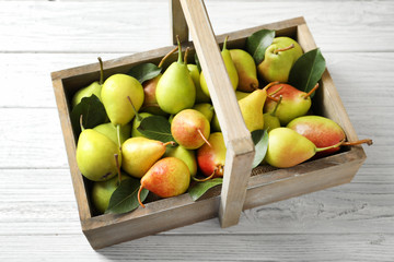 Ripe pears in wooden basket on light background