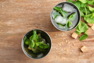 Two metal glasses with mint julep on wooden table