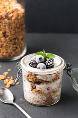 Granola with yogurt, blueberries and blackberries in a glass on a black background, selective focus, vertical