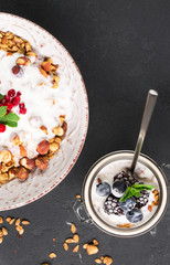 Granola with yoghurt, blueberries and blackberries in a white plate on a black background, selective focus, vertical