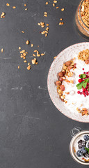 Granola with yoghurt, blueberries and blackberries in a white plate on a black background, selective focus, vertical