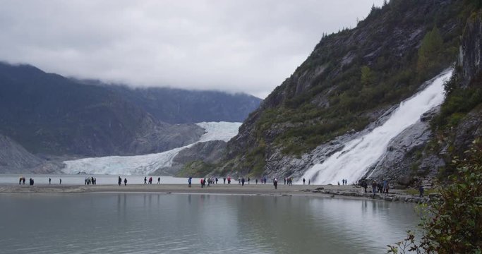 Alaska glacier landscape - tourists visiting Mendenhall Glacier tourist attraction. People in front of famous cruise shore excursion near Juneau. Nugget Falls waterfall on right. RED EPIC SLOW MOTION.