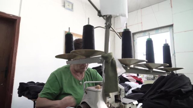 Caucasian girl sitting using sewing machine to stitching factory textile, close up, shallow depth of field, young female person tailoring, interior scene