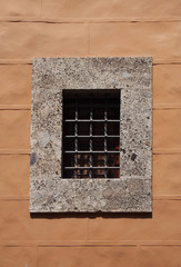 concrete window frame with thick security metal bars in a yellow painted stone wall