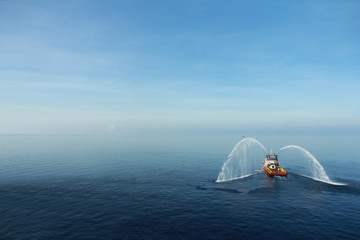 Fire hose boat is spraying water on the sea for supporting emergency case of fire of offshore oil and gas industry. Fire fighting boat sprays water on the sea.