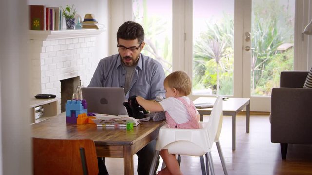 Father working from home while baby plays with toys