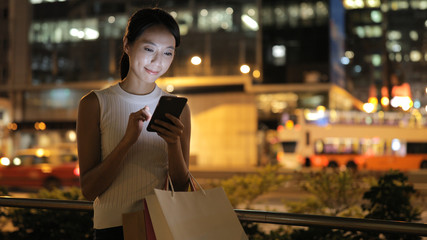 Woman using smart phone and holding shopping bag