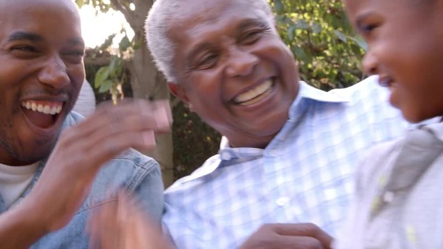 Young black boy playing with dad, uncle and grandad outdoors