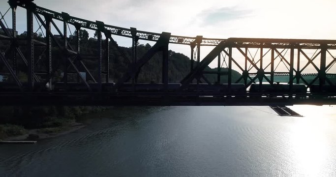 A silhouetted aerial shot of a cargo train traveling over a railroad bridge spanning the Ohio River.  	
