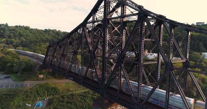 A dynamic rising aerial establishing shot of a cargo trail traveling on a railroad bridge over the Ohio River in Western Pennsylvania.  	