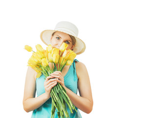 Woman in a hat peeks out from behind a bouquet of yellow spring tulips.