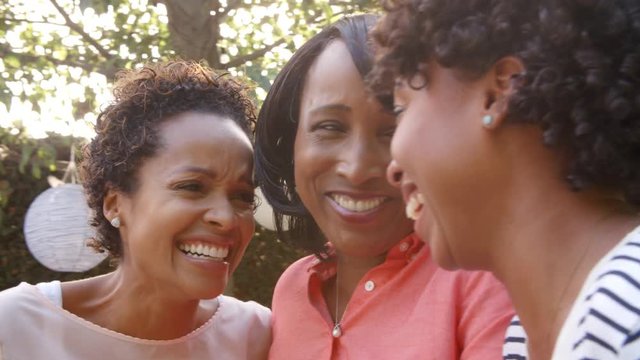 Black mother and adult daughters talking in garden, close up