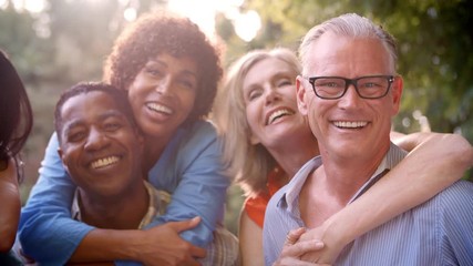 Mature Friends Giving Piggybacks In Backyard Together - Powered by Adobe