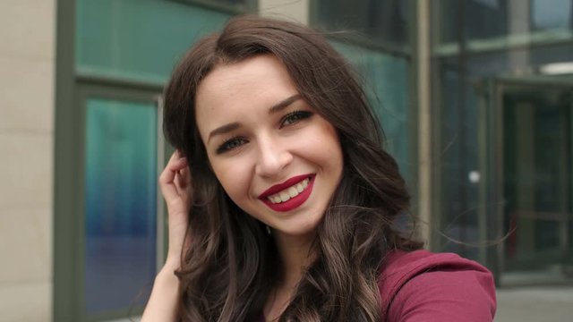 Portrait of a girl making a selfie close-up. Shooting from first person. Close-up selfie-portrait of pretty girl with long dark hair on street at city urban background. 4K