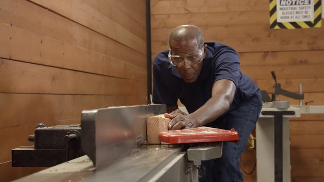 Male Carpenter Using Plane In Woodworking Woodshop