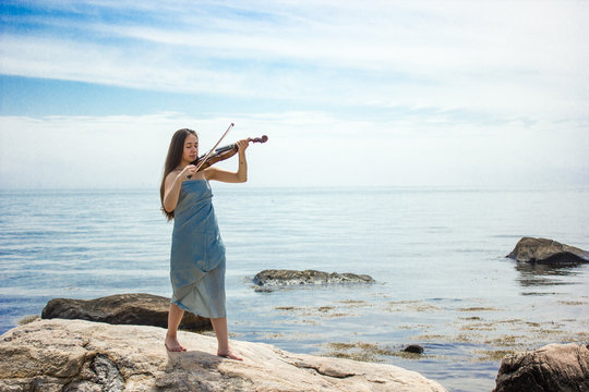girl in blue playing violin by ocean