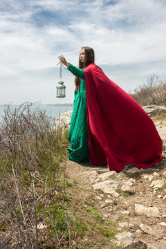 girl by ocean with lantern and red cape
