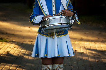 Girl drummer holds a drum and drum sticks in hand at the parade on the street.
