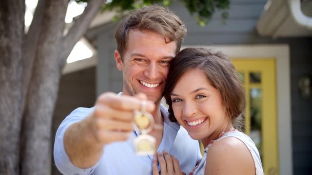 Portrait Of Happy Couple Standing Outside New Home With Keys