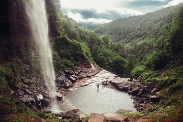 Scenic view on mountain waterfall and cave in forest with tourist people. Kaaterskill Falls and Clove..