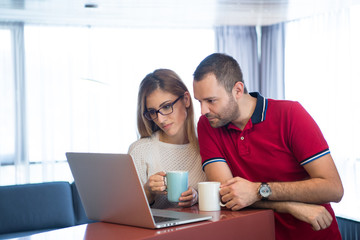 couple drinking coffee and using laptop at home