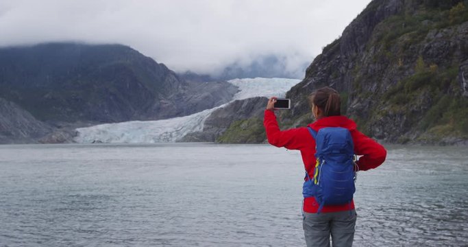 Hiking tourist on Alaska travel taking photo of glacier. Woman tourist taking picture using smart phone on vacation. Mendenhall Glacier. RED EPIC SLOW MOTION