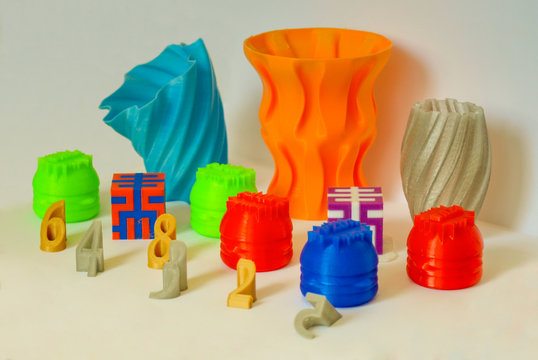 Models printed by 3d printer. Bright colorful objects printed on 3d printer on table.Automatic three dimensional printer performs plastic modeling in laboratory. Progressive modern additive technology