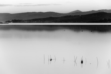 A lake at dusk, with soft light, distant hills and mountains, fishing nets in the foreground an a lot of empty space - 173174771