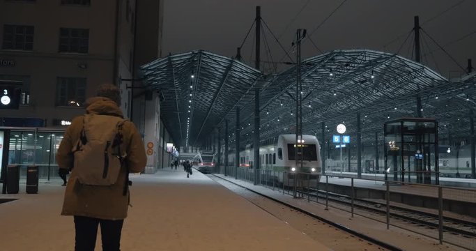 HELSINKI, FINLAND - JANUARY 07, 2017: Central railway station at winter night. Passenger train leaving and man (with model release) taking mobile video of moving transport