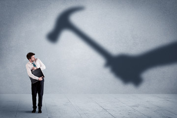 Business person afraid of a shadow hand holding hammer concept