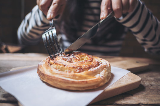 A woman cutting a piece of raisin danish with fork and knife on wooden plate in vintage cafe