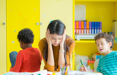Teacher get headache with two naughty kids in classroom at kindergarten school.